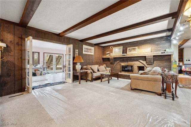 carpeted living room with beam ceiling, a fireplace, a textured ceiling, french doors, and wood walls