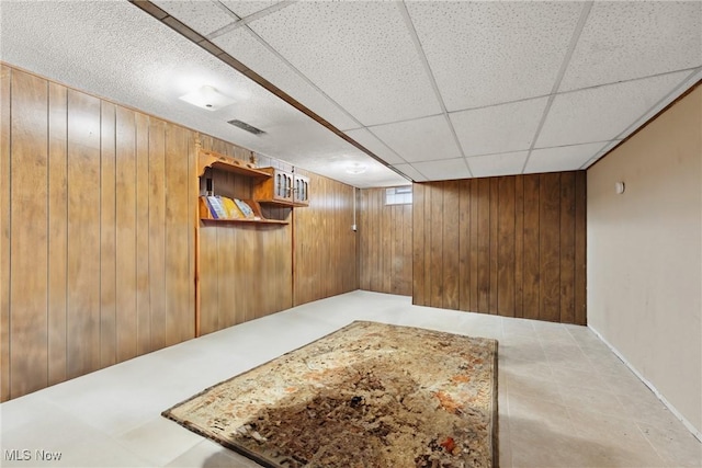 basement with wooden walls and a paneled ceiling