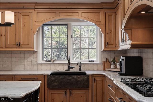 kitchen featuring light stone counters, sink, backsplash, and black gas cooktop