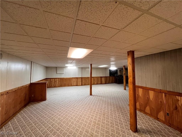 basement featuring a paneled ceiling, carpet, and wood walls