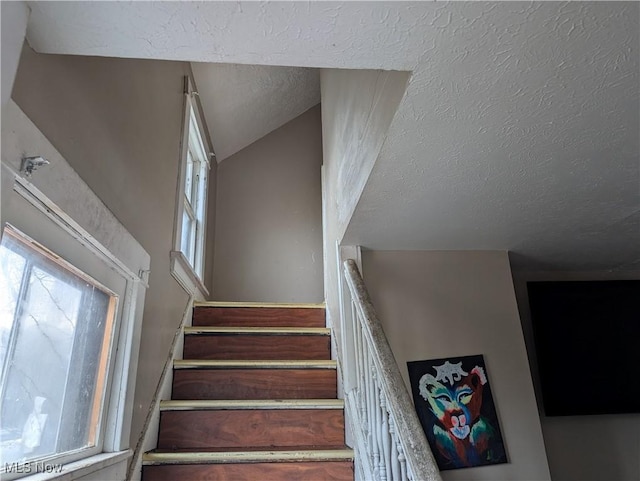 staircase featuring vaulted ceiling and a textured ceiling