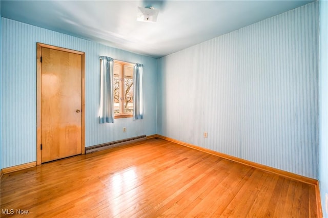 unfurnished room with a baseboard heating unit and light hardwood / wood-style flooring