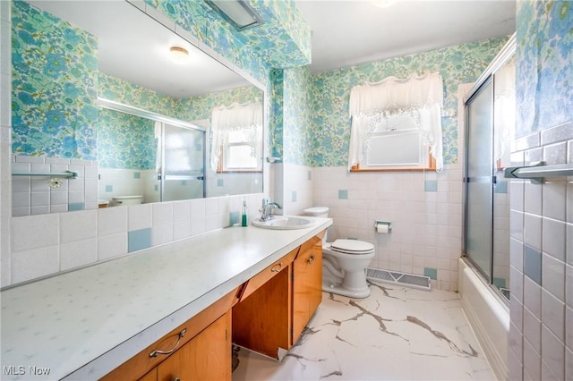 full bathroom featuring vanity, tile walls, shower / bath combination with glass door, and toilet