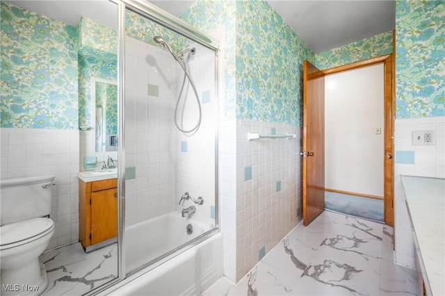 full bathroom featuring vanity, toilet, combined bath / shower with glass door, and tile walls