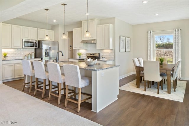 kitchen with stainless steel appliances, sink, a kitchen island with sink, and hanging light fixtures