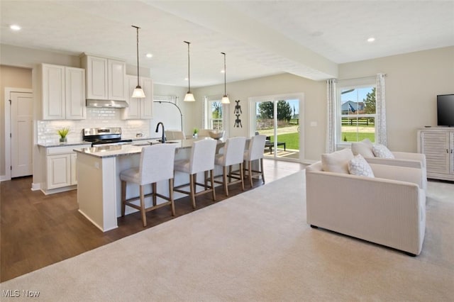 kitchen with a kitchen island with sink, hanging light fixtures, backsplash, white cabinets, and stainless steel electric stove