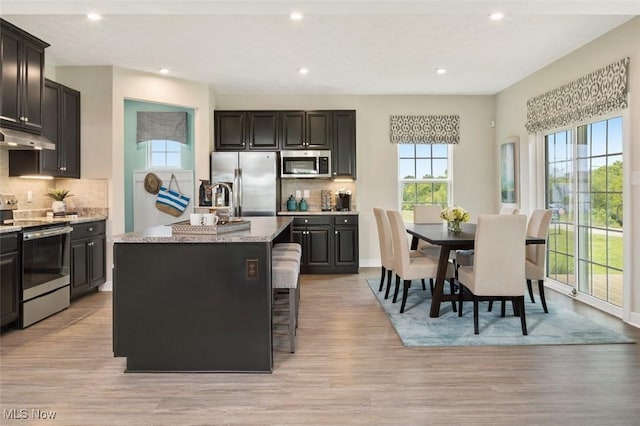 kitchen featuring light stone counters, stainless steel appliances, an island with sink, and light wood-type flooring