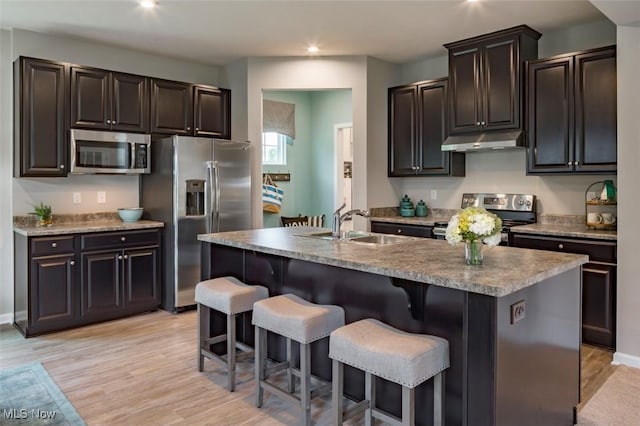 kitchen featuring a kitchen island with sink, sink, stainless steel appliances, and light hardwood / wood-style floors