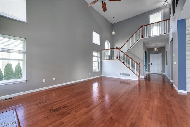 unfurnished living room with hardwood / wood-style floors, ceiling fan, and a high ceiling