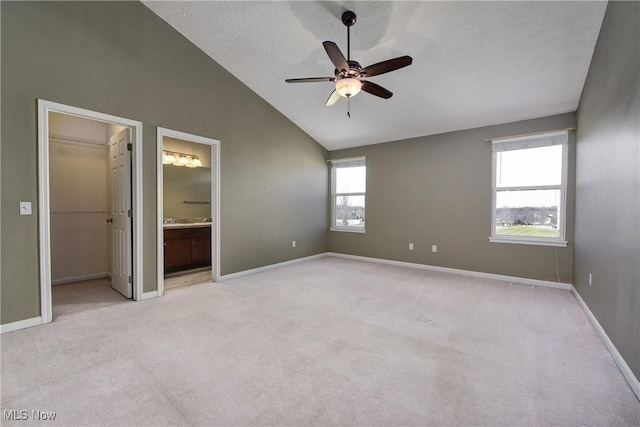 unfurnished bedroom with vaulted ceiling, a spacious closet, light colored carpet, ceiling fan, and a textured ceiling