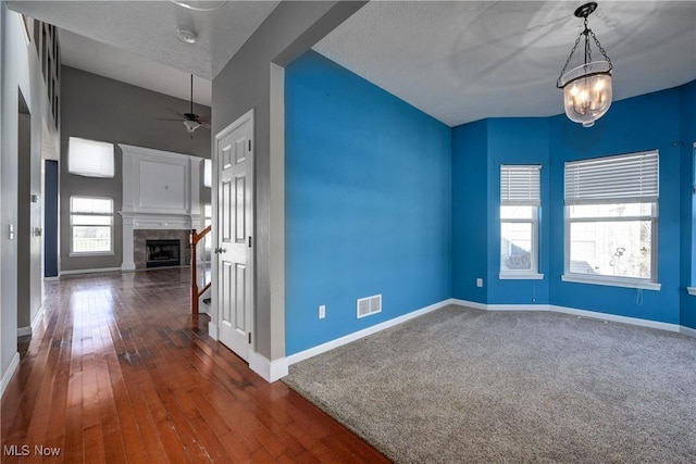 empty room featuring a tile fireplace, dark wood-type flooring, and ceiling fan with notable chandelier