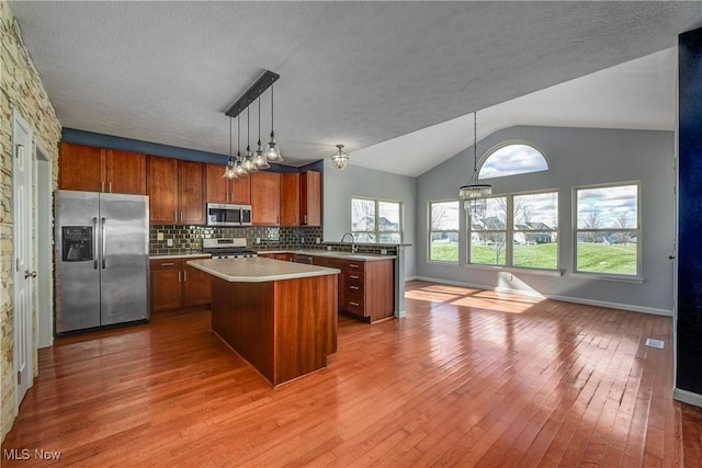 kitchen with hanging light fixtures, light hardwood / wood-style flooring, a kitchen island, stainless steel appliances, and backsplash