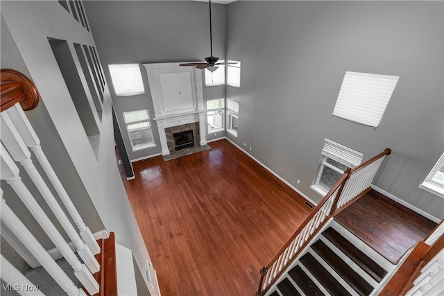 unfurnished living room with ceiling fan, a fireplace, dark hardwood / wood-style flooring, and a high ceiling