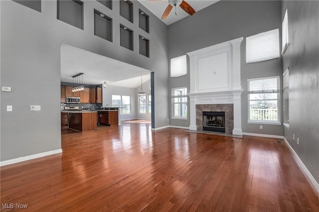 unfurnished living room with ceiling fan, dark hardwood / wood-style floors, a tile fireplace, and a towering ceiling