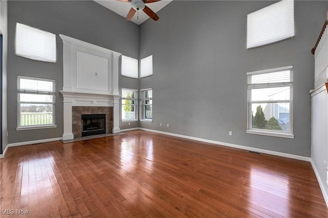 unfurnished living room with ceiling fan, a towering ceiling, a fireplace, and hardwood / wood-style floors