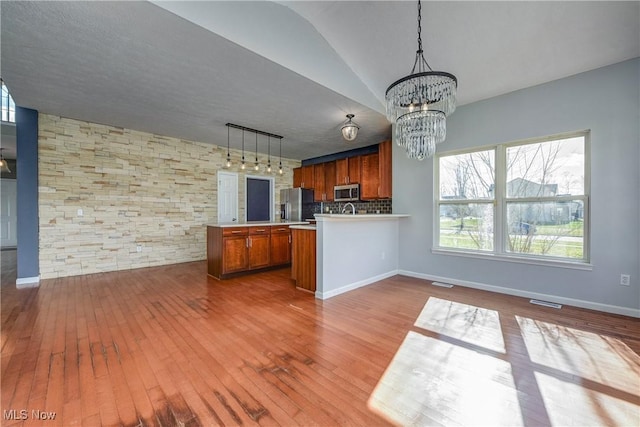 kitchen featuring decorative light fixtures, stainless steel appliances, kitchen peninsula, and hardwood / wood-style flooring