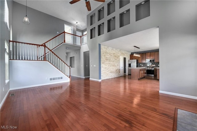 unfurnished living room featuring dark wood-type flooring, ceiling fan, and a high ceiling