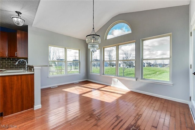 unfurnished dining area featuring vaulted ceiling, a healthy amount of sunlight, sink, and light wood-type flooring