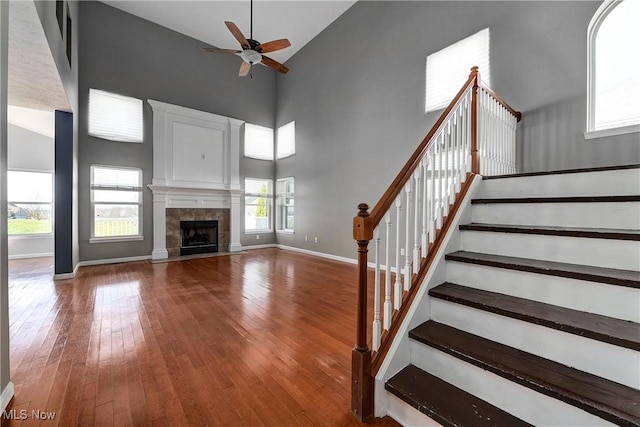 unfurnished living room with hardwood / wood-style flooring, a towering ceiling, ceiling fan, and a tile fireplace