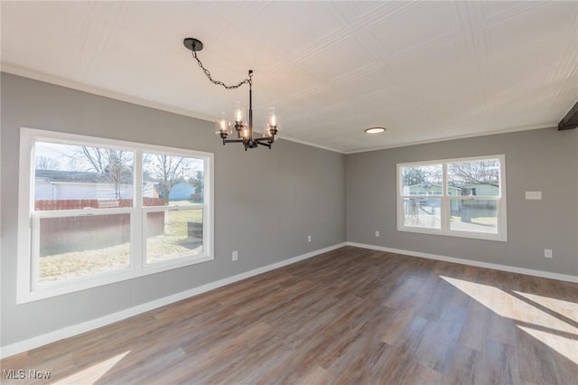 spare room with a notable chandelier, wood-type flooring, ornamental molding, and a wealth of natural light