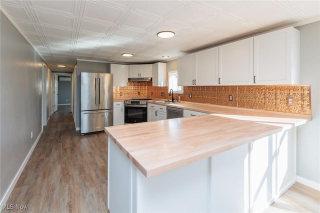 kitchen with hardwood / wood-style floors, white cabinets, decorative backsplash, kitchen peninsula, and stainless steel appliances