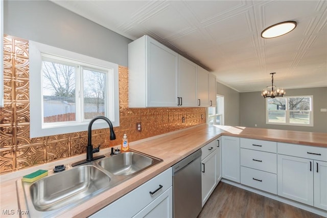 kitchen with butcher block counters, sink, white cabinetry, hanging light fixtures, and stainless steel dishwasher