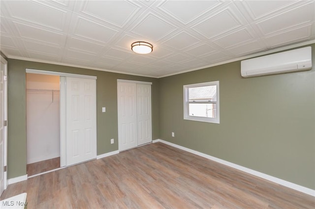 unfurnished bedroom with light hardwood / wood-style floors, an AC wall unit, and multiple closets