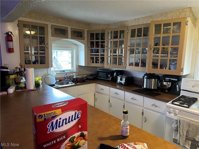 kitchen featuring white gas range, a textured ceiling, sink, and white cabinets