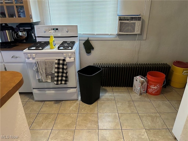 kitchen with white cabinets, radiator heating unit, white gas stove, and light tile patterned floors