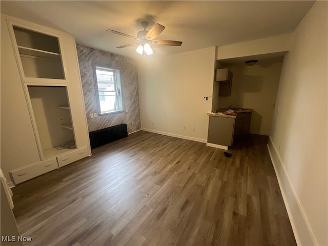 unfurnished living room featuring dark wood-type flooring, ceiling fan, and radiator heating unit