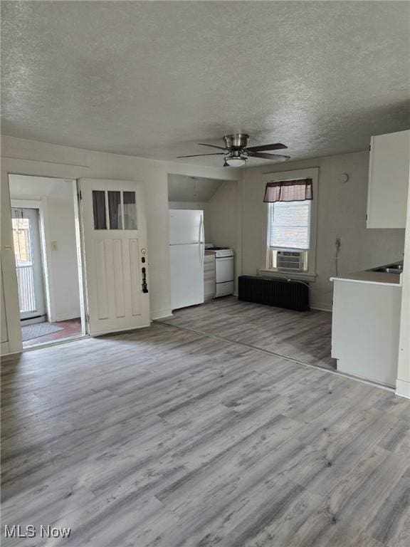 unfurnished living room featuring ceiling fan, radiator heating unit, washer and dryer, a textured ceiling, and light wood-type flooring