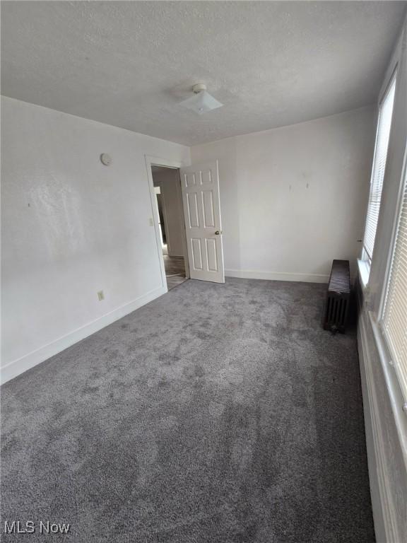 unfurnished room with a textured ceiling and dark carpet