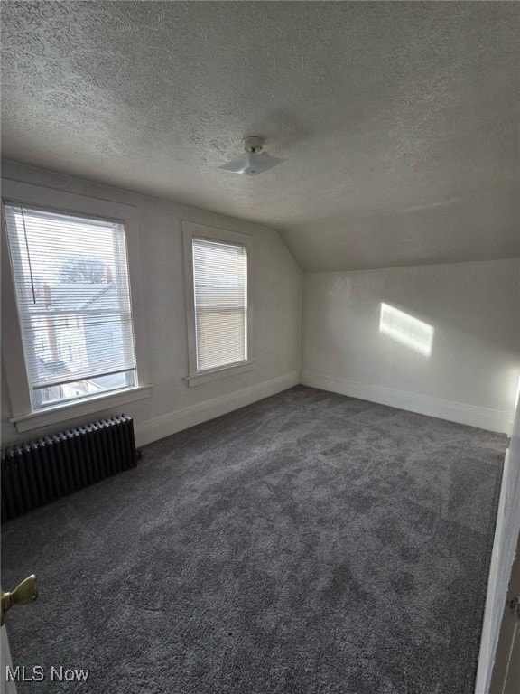 additional living space featuring lofted ceiling, dark colored carpet, a textured ceiling, radiator heating unit, and ceiling fan