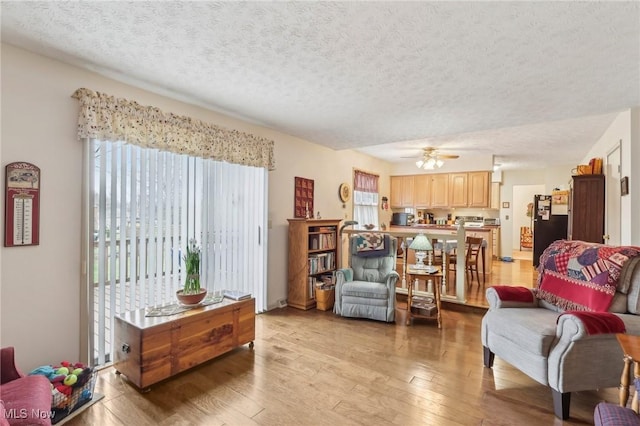 living room featuring ceiling fan, a textured ceiling, and light wood-type flooring