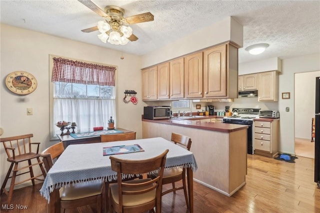 kitchen featuring a textured ceiling, light brown cabinets, ceiling fan, gas range oven, and light hardwood / wood-style floors