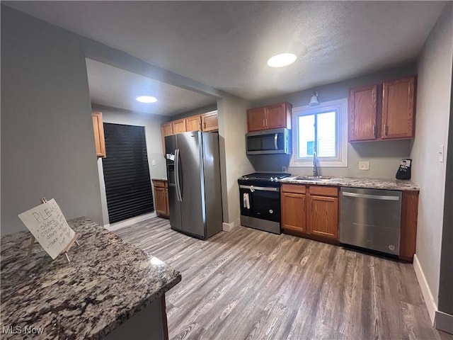 kitchen featuring hardwood / wood-style flooring, appliances with stainless steel finishes, light stone countertops, and sink