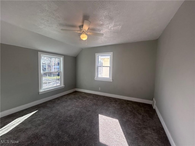 carpeted empty room featuring ceiling fan, vaulted ceiling, and a textured ceiling