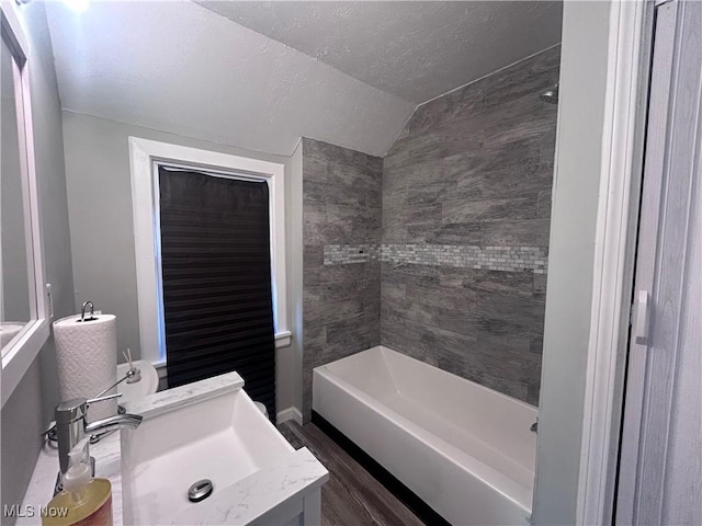 bathroom featuring hardwood / wood-style flooring, vanity, a textured ceiling, vaulted ceiling, and tiled shower / bath