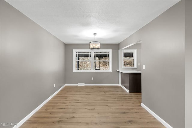 unfurnished dining area with a textured ceiling, a chandelier, and light hardwood / wood-style flooring