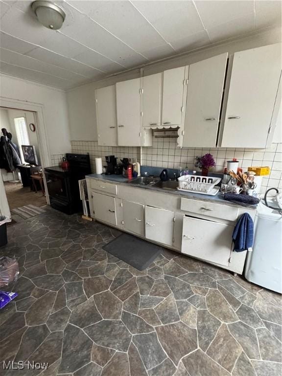 kitchen with black / electric stove, backsplash, and white cabinets