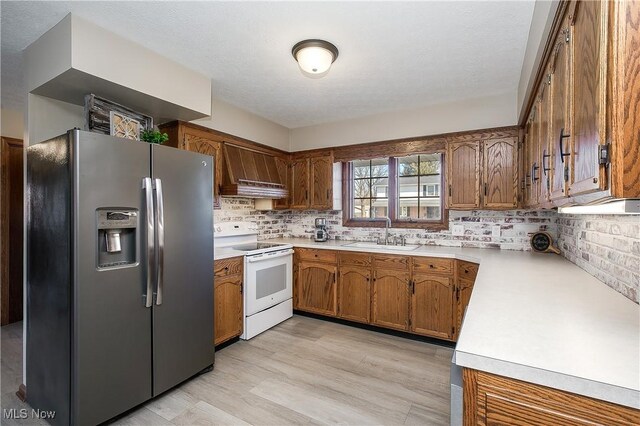 kitchen featuring premium range hood, white range with electric stovetop, sink, stainless steel fridge, and decorative backsplash