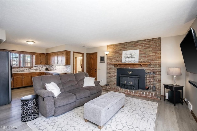 living room featuring sink, a textured ceiling, a brick fireplace, and light wood-type flooring