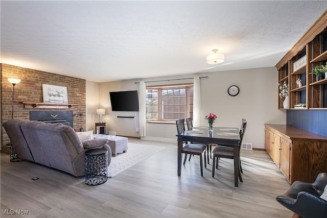 living room with a brick fireplace, a textured ceiling, and light hardwood / wood-style flooring