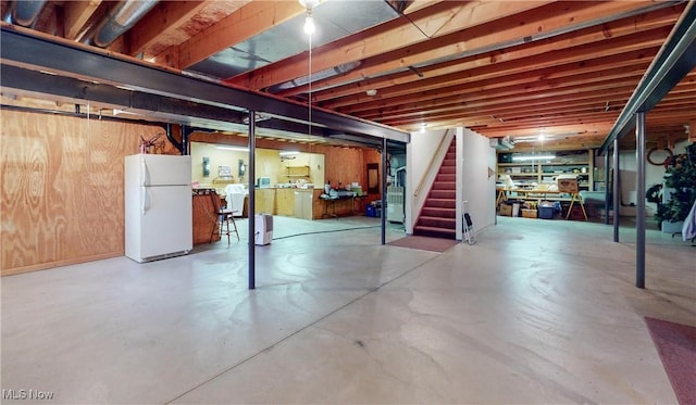 basement featuring white refrigerator, washer / dryer, heating unit, and wood walls