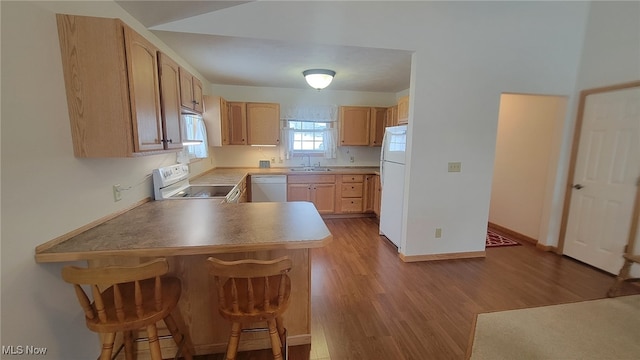 kitchen featuring a breakfast bar, sink, light brown cabinets, kitchen peninsula, and white appliances