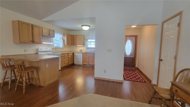 kitchen with a breakfast bar, light brown cabinets, white appliances, and kitchen peninsula