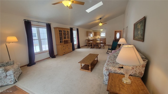 carpeted living room with ceiling fan, a skylight, and high vaulted ceiling