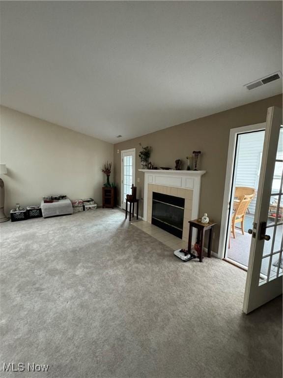 unfurnished living room featuring a tiled fireplace, visible vents, and carpet