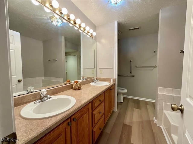 721 Winding Way, Akron, OH 44313 - bathroom featuring a textured ceiling, wood finished floors, double vanity, toilet, and a tub to relax in