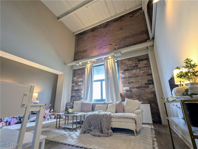 living area with a towering ceiling, hardwood / wood-style flooring, beamed ceiling, and brick wall